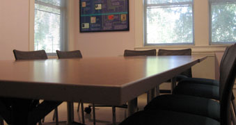 Conference room table with five chairs around it and windows to the quad in the background
