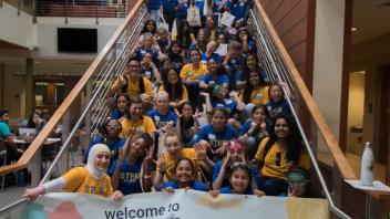 2018 Stem for Girls group sitting on stairs holding Stem for Girls Banner making funny faces. 